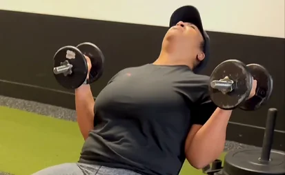 Woman performing a dumbbell chest press during an upper body strength workout at the gym